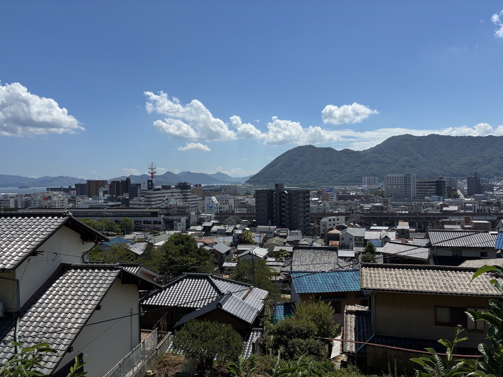 大島神社の高台から見た三原の町並み。瓦屋根の向こうに市街地と山が見えます