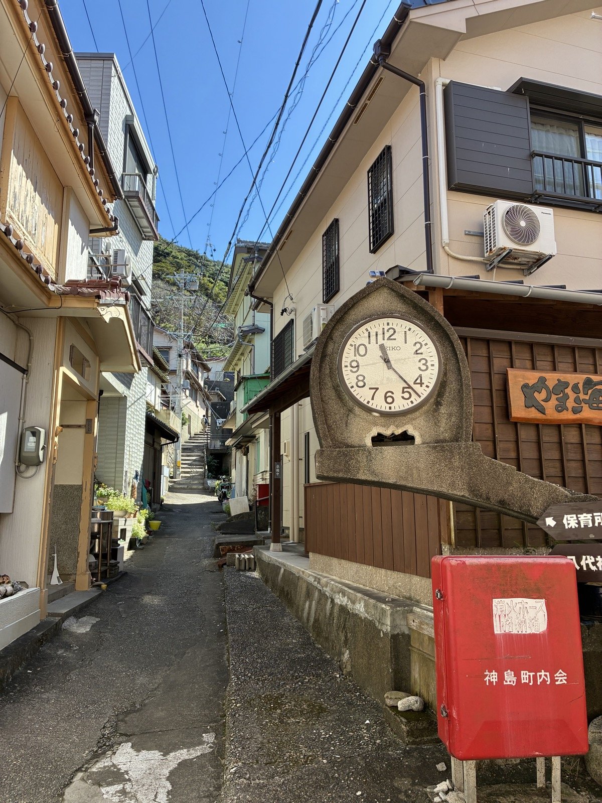 神島の集落の路地の角に立つ石の時計台